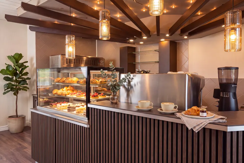 Theke des Cafés mit Vitrine voller Gipfeli, Tartes und Torten, zwei Cappuccini und der Kaffeemaschine unter Holzbalken (Symbolbild auf Basis einer Aufnahme des Lokals)